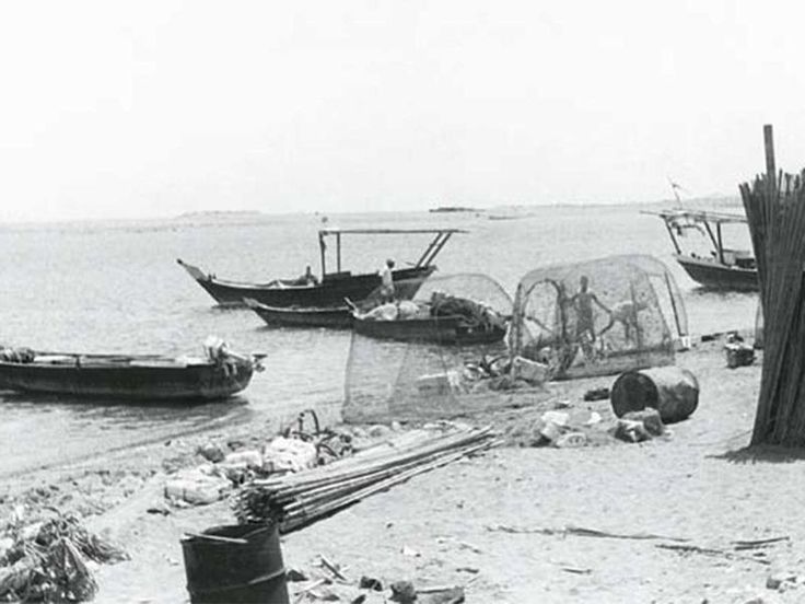 black and white photograph of fishing nets on the beach with other boats in the water