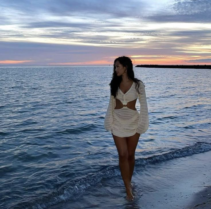 a woman walking on the beach at sunset