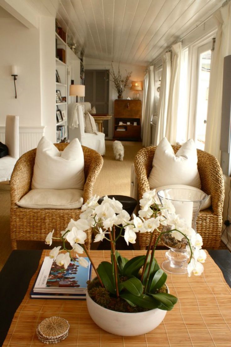 a living room with wicker furniture and white flowers on the coffee table in front of two couches