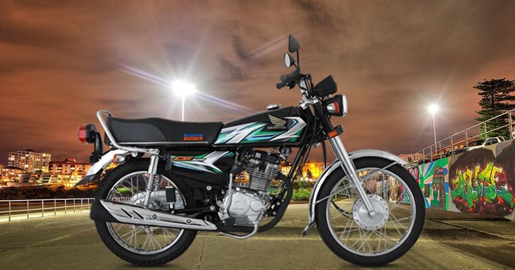 a motorcycle parked on the side of a road at night with lights in the background