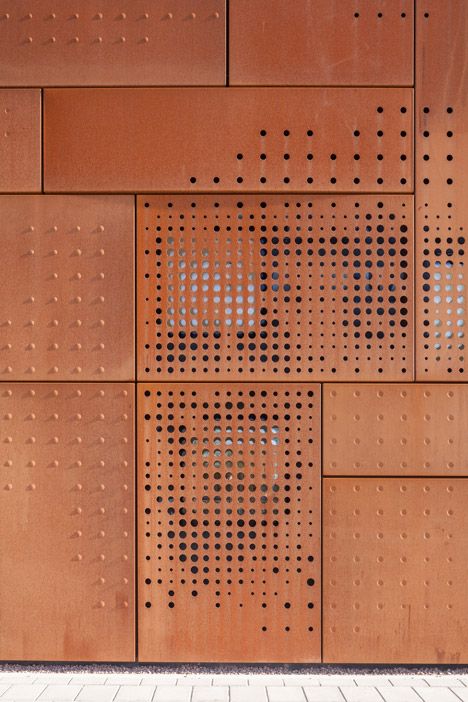 a woman walking down the street in front of a building with perfored metal panels on it