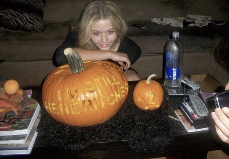 a woman sitting in front of a pumpkin carved to look like it has writing on it