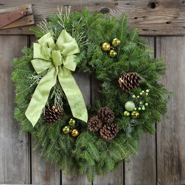 a green wreath with pine cones and ornaments