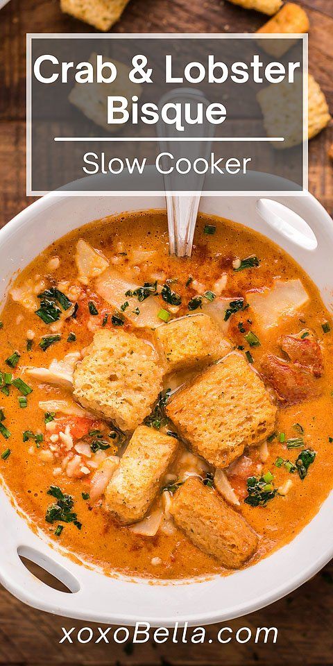 a bowl of crab and lobster bisque with crackers on the side, in front of a wooden table