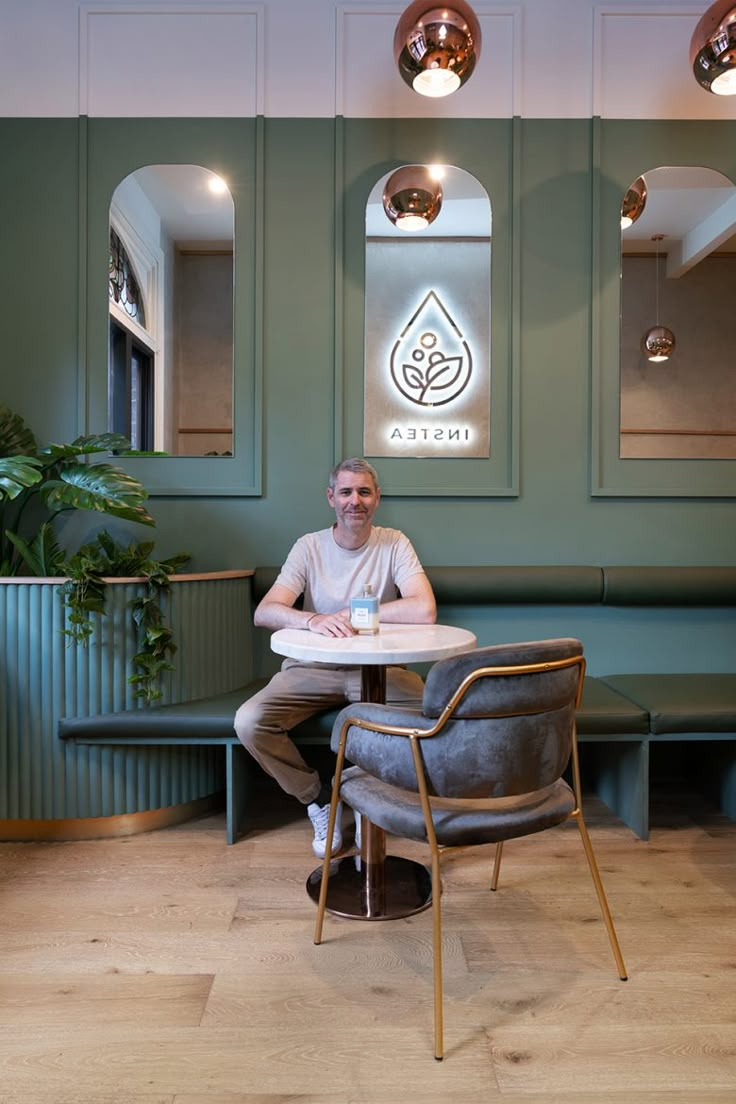 a man sitting at a table in front of a green wall with an emblem on it