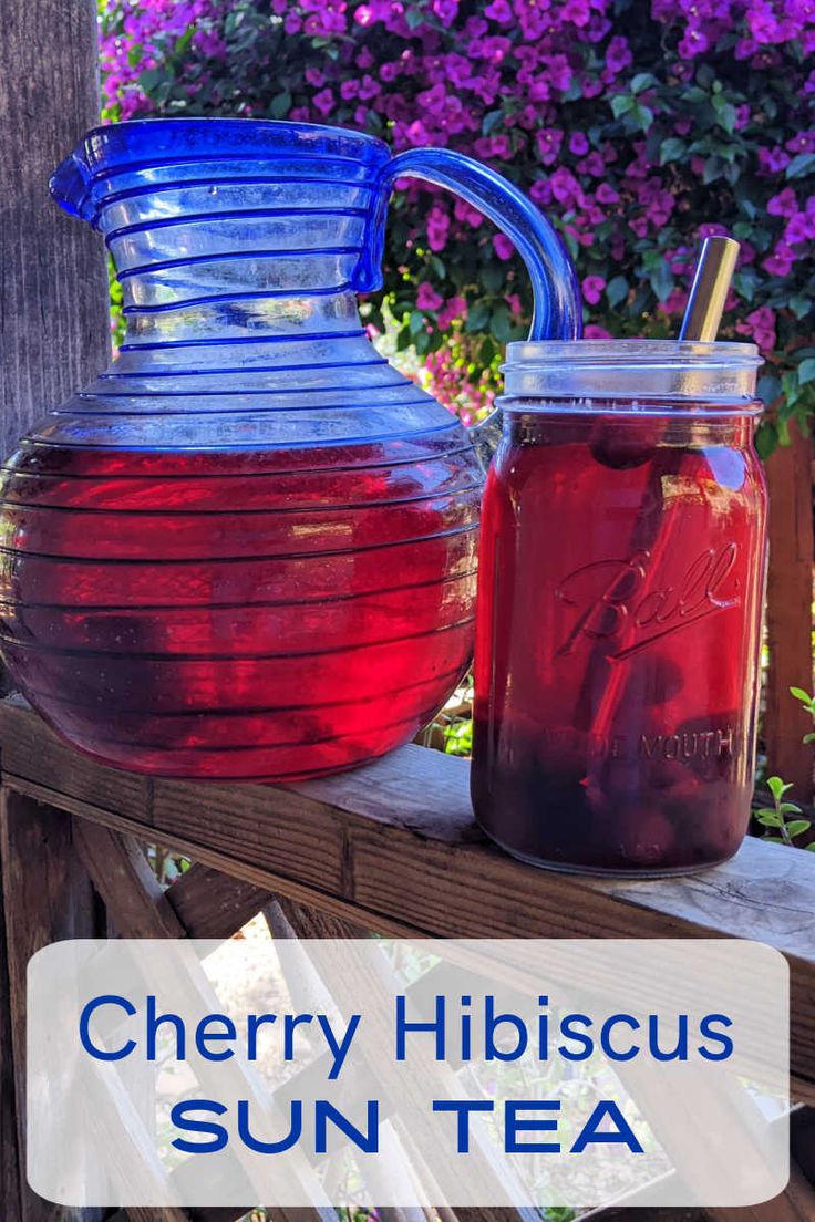 two jugs filled with liquid sitting on top of a wooden table next to purple flowers