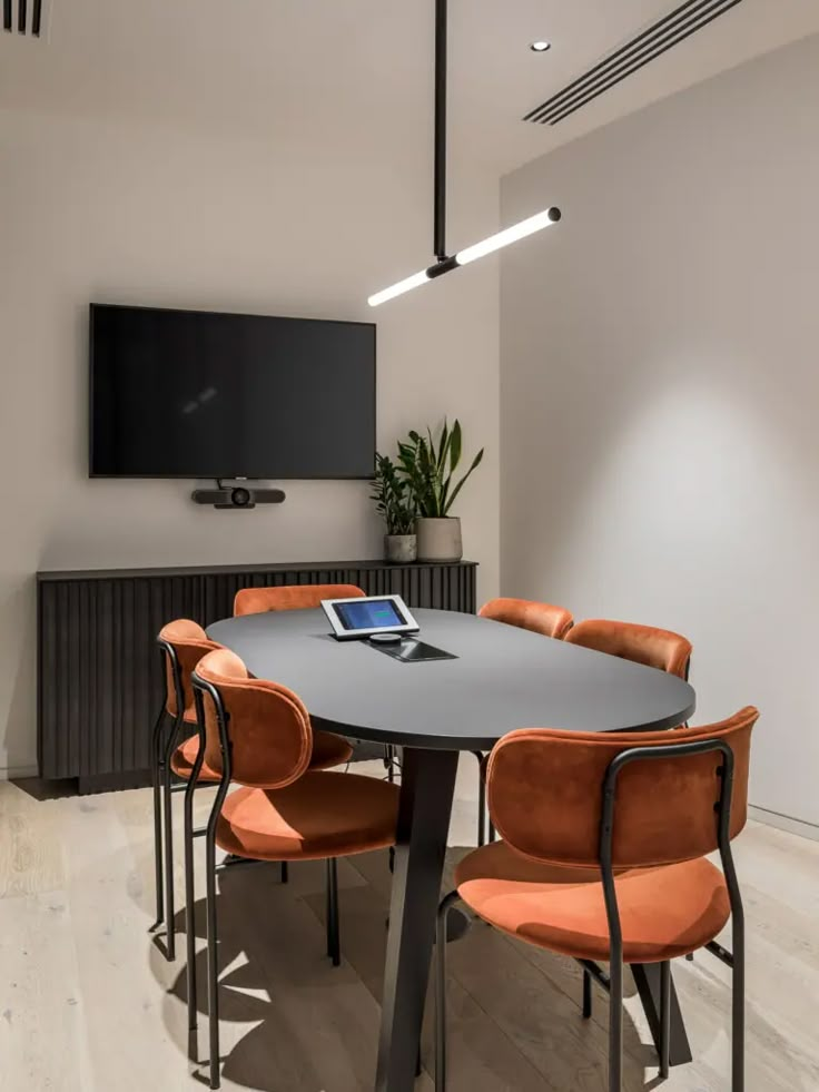 an office meeting room with orange chairs and a flat screen tv mounted on the wall