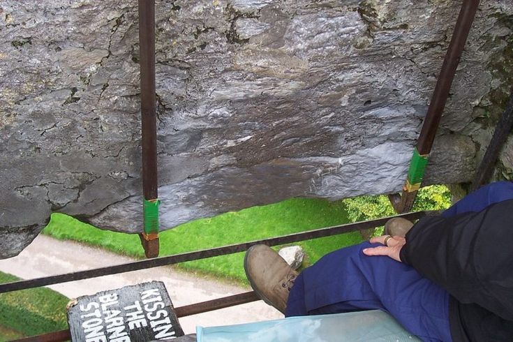 a man sitting on top of a metal bench next to a stone wall and green grass