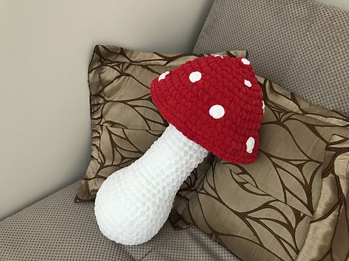 a red and white knitted mushroom sitting on top of a pillow