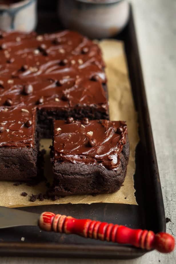 a chocolate cake on a tray with a knife next to it and two cups in the background