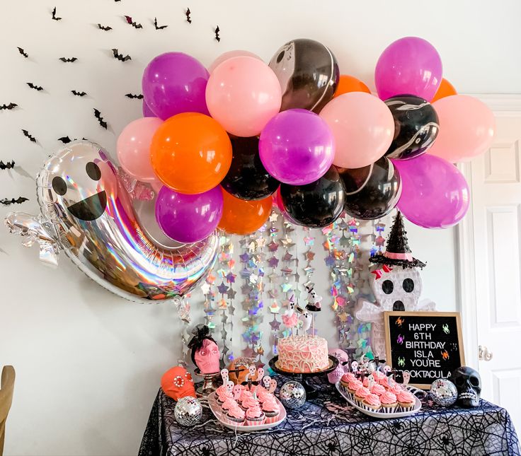 a table topped with lots of balloons and desserts next to a halloween themed wall