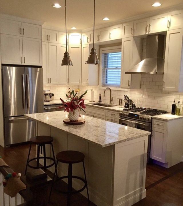 a kitchen with white cabinets and an island in the middle is lit by three pendant lights