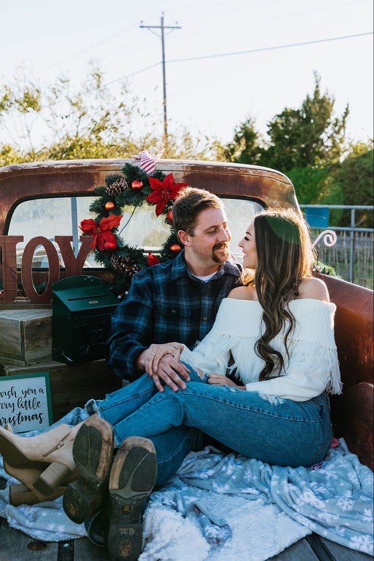 a man and woman sitting in the back of an old truck with christmas wreaths on it