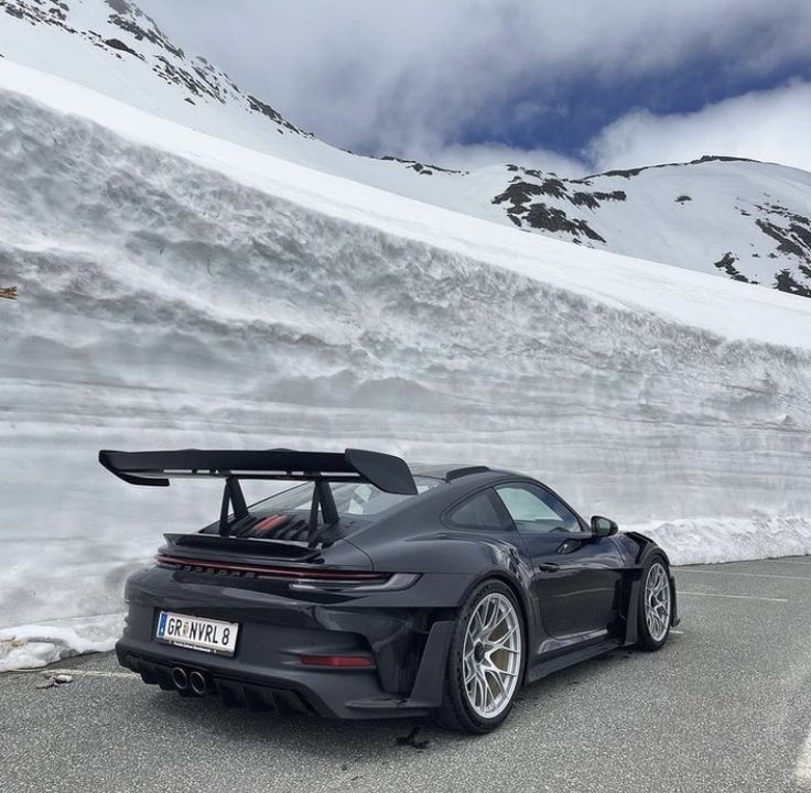 a black porsche sports car parked on the side of a road with snow covered mountains in the background