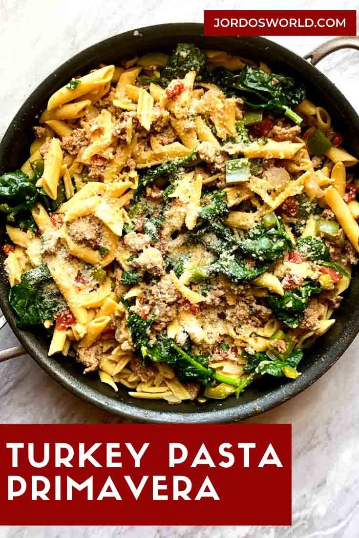 a skillet filled with pasta and spinach covered in sauce on top of a marble counter