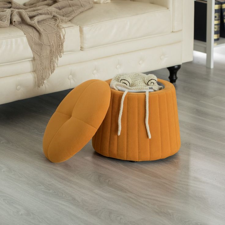 an orange stool sitting on top of a wooden floor next to a white couch and ottoman