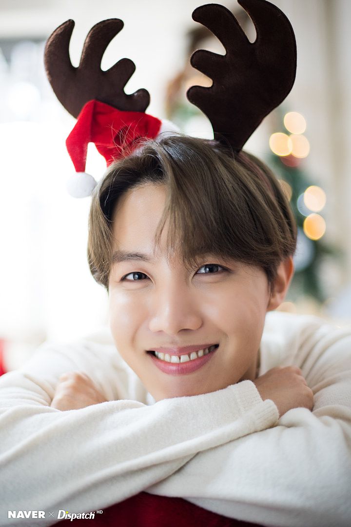 a woman with reindeer antlers on her head smiles for the camera while sitting in front of a christmas tree