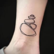 a black and white photo of a pebble stone tattoo on the ankle