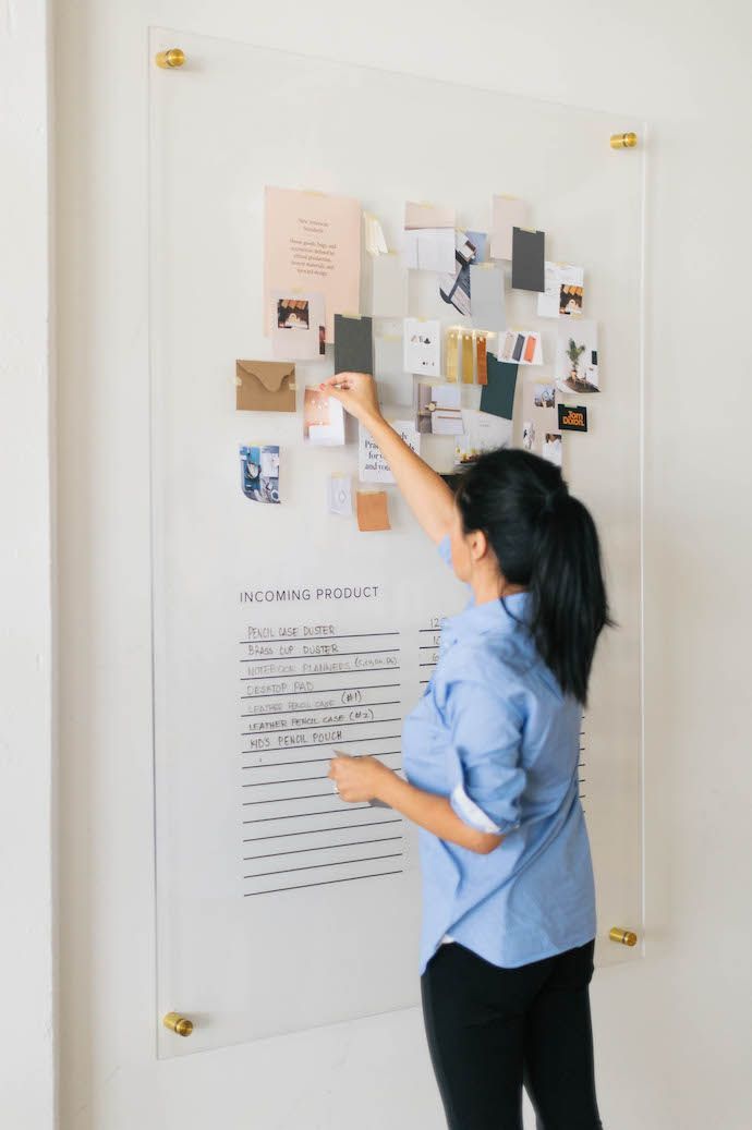 a woman standing in front of a white board with magnets on it and papers pinned to the wall