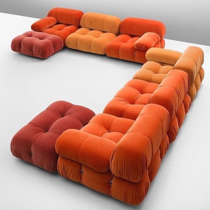 an orange and red couch sitting on top of a white table next to each other