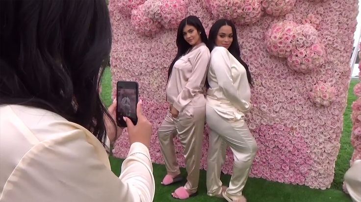 two women standing next to each other in front of a wall covered with pink flowers