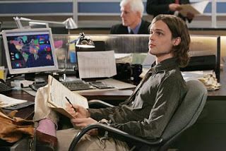 a man sitting at a desk in front of a computer monitor and holding a book