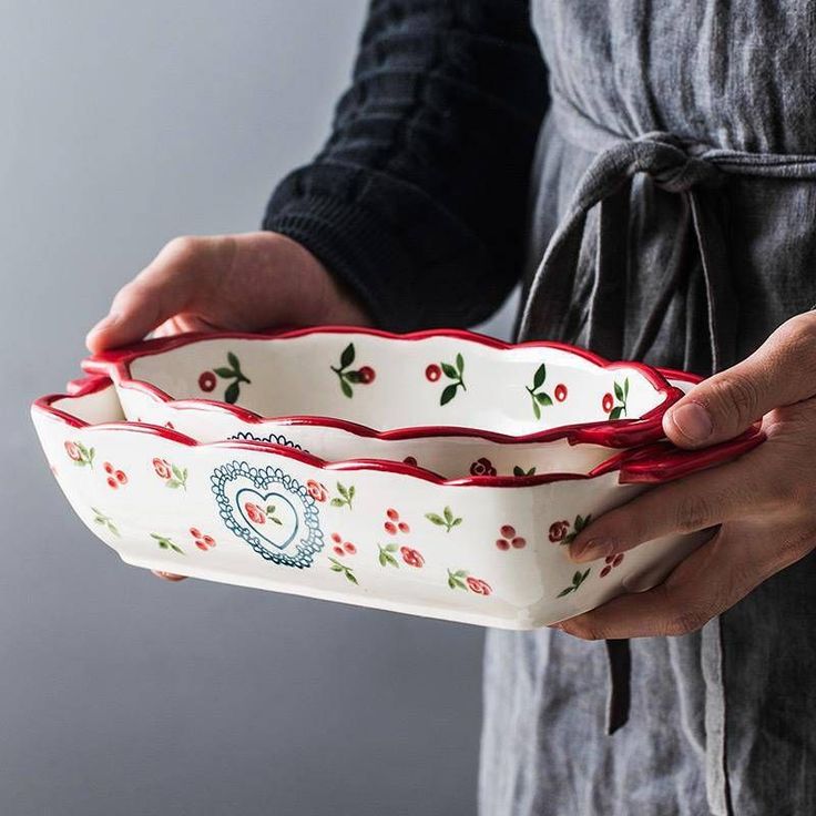 a person is holding two bowls in their hands, one has red handles and the other has green leaves on it