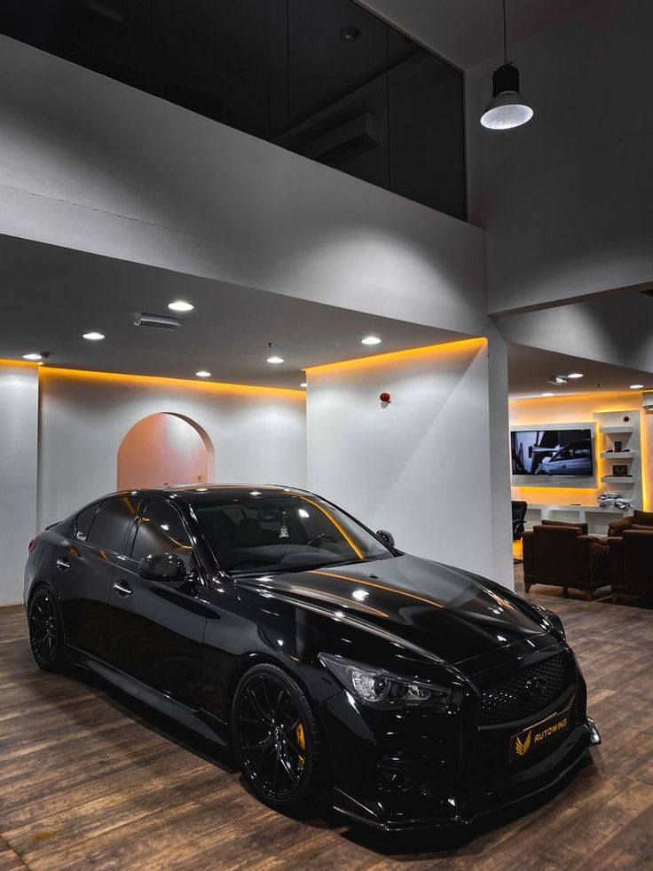 a black sports car is parked in a showroom with wood flooring and white walls