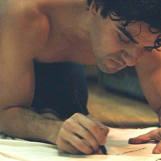 a shirtless man writing on a piece of paper