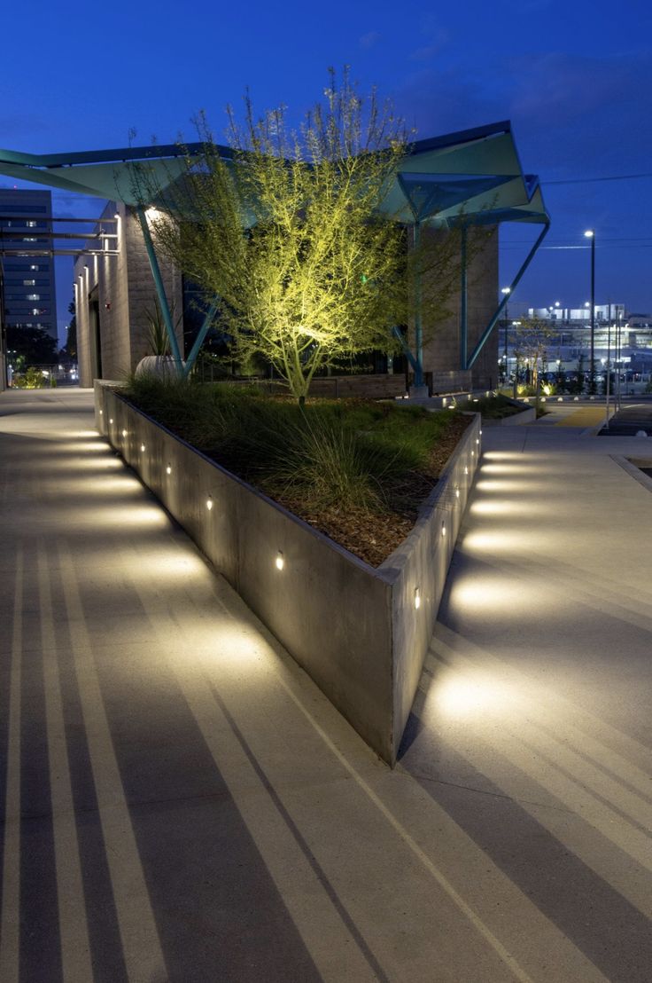 an outdoor area with concrete planters and lights on the side of it at night