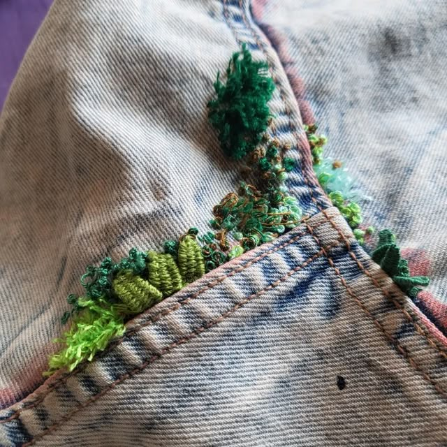 a pair of jeans with embroidered trees on the side and green leaves sticking out of them