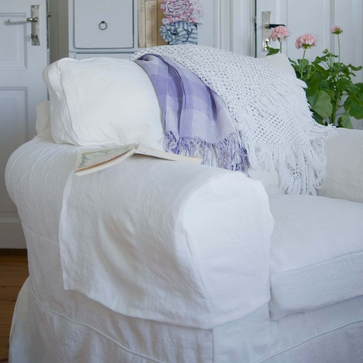 a white couch covered in pillows and blankets next to a potted plant with pink flowers