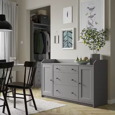 a dining room table with four chairs next to a dresser and hanging pictures on the wall