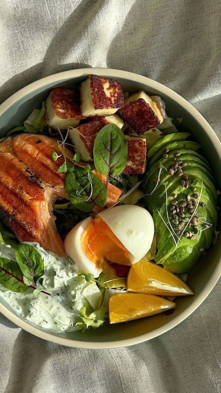 a bowl filled with salad and meat on top of a bed of white linens