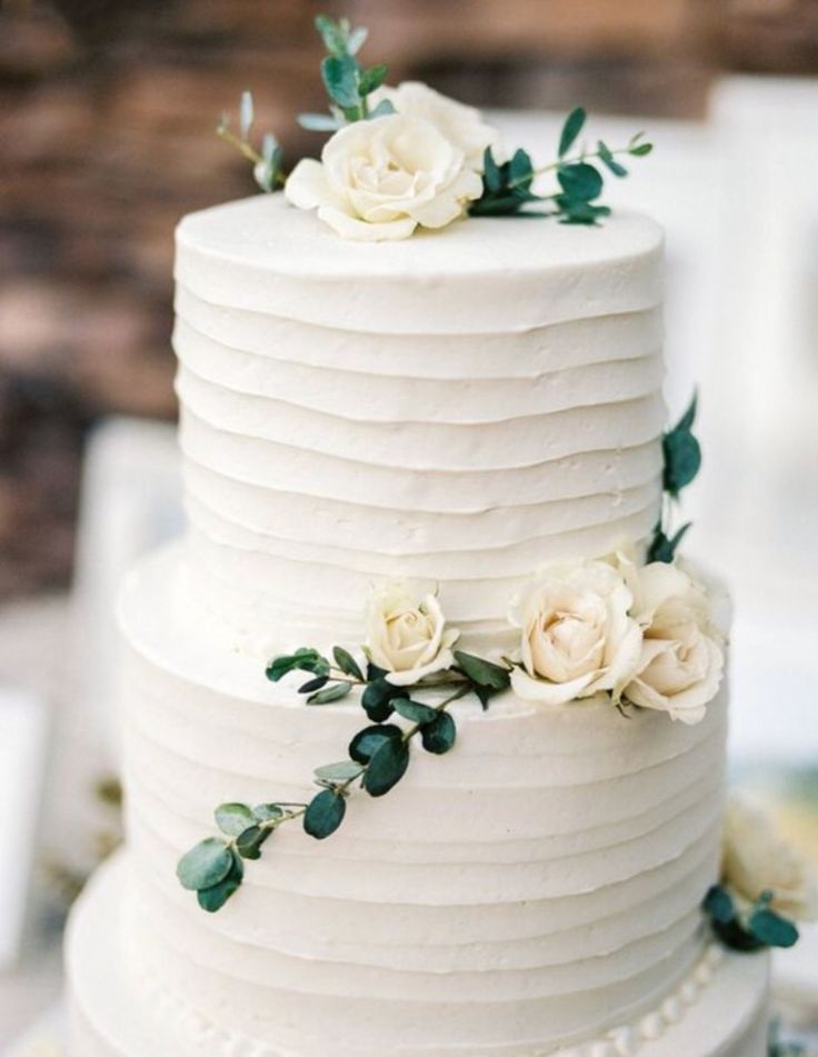 a white wedding cake with flowers and greenery on the top is sitting on a table