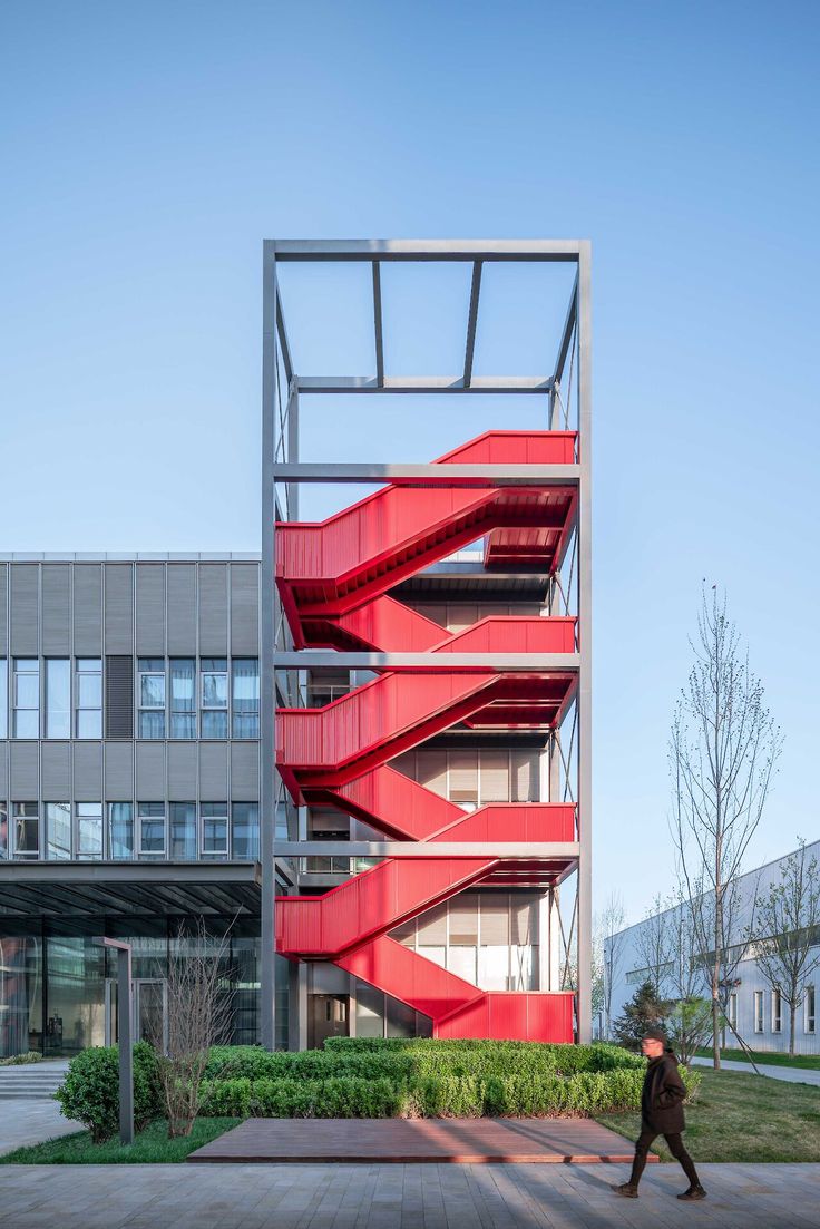 a man walking past a tall red staircase in front of a building with glass windows