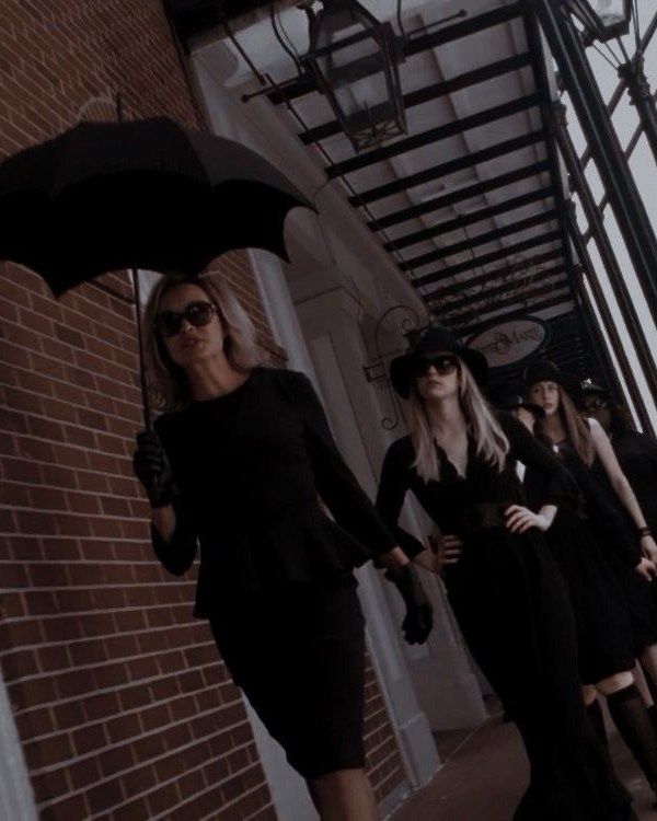 three women in black dresses and hats are walking down the street with their umbrellas open