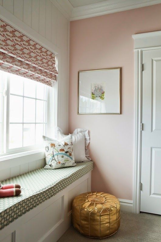 a room with pink walls and white trim on the window sill is decorated with gold accents