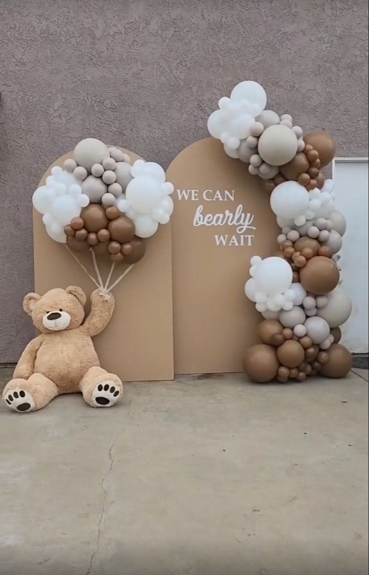 a teddy bear sitting in front of a balloon arch that says we can be really wait