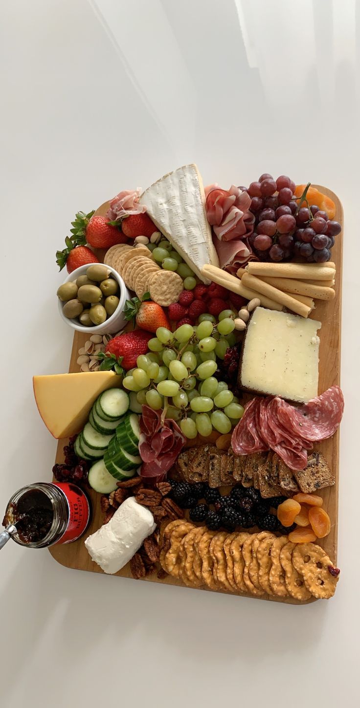 an assortment of cheeses, meats, and fruit on a wooden platter