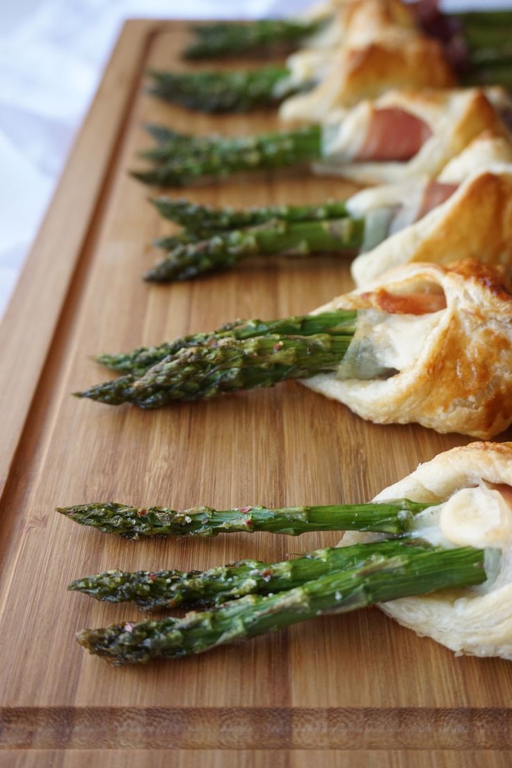 asparagus and ham wrapped in puff pastry on a cutting board with other food items