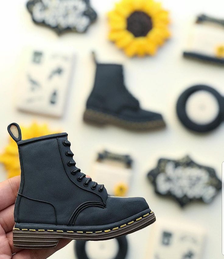 a person holding up a pair of black shoes in front of some sunflowers