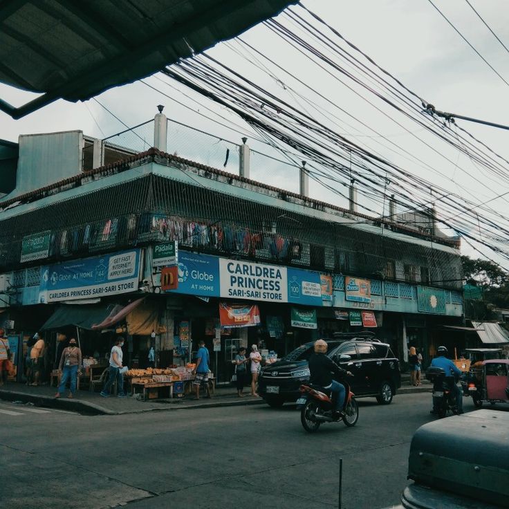 people are standing on the street corner in front of a building with many wires above it