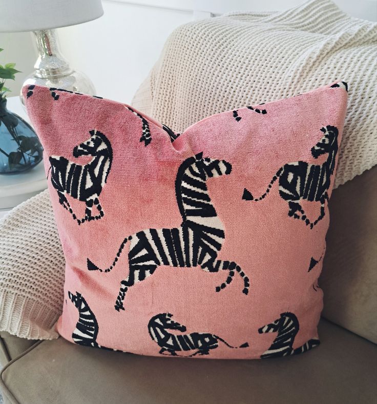 a pink pillow with zebras on it sitting on a chair next to a lamp