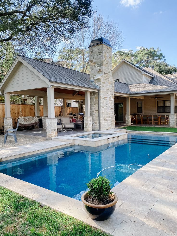 a backyard with a pool, patio and fireplace in the middle of it is surrounded by greenery