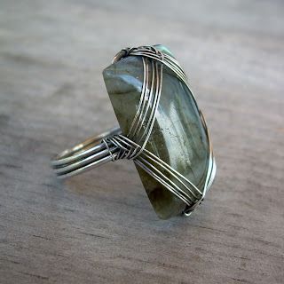 a large green stone ring sitting on top of a wooden table with wire wrapped around it