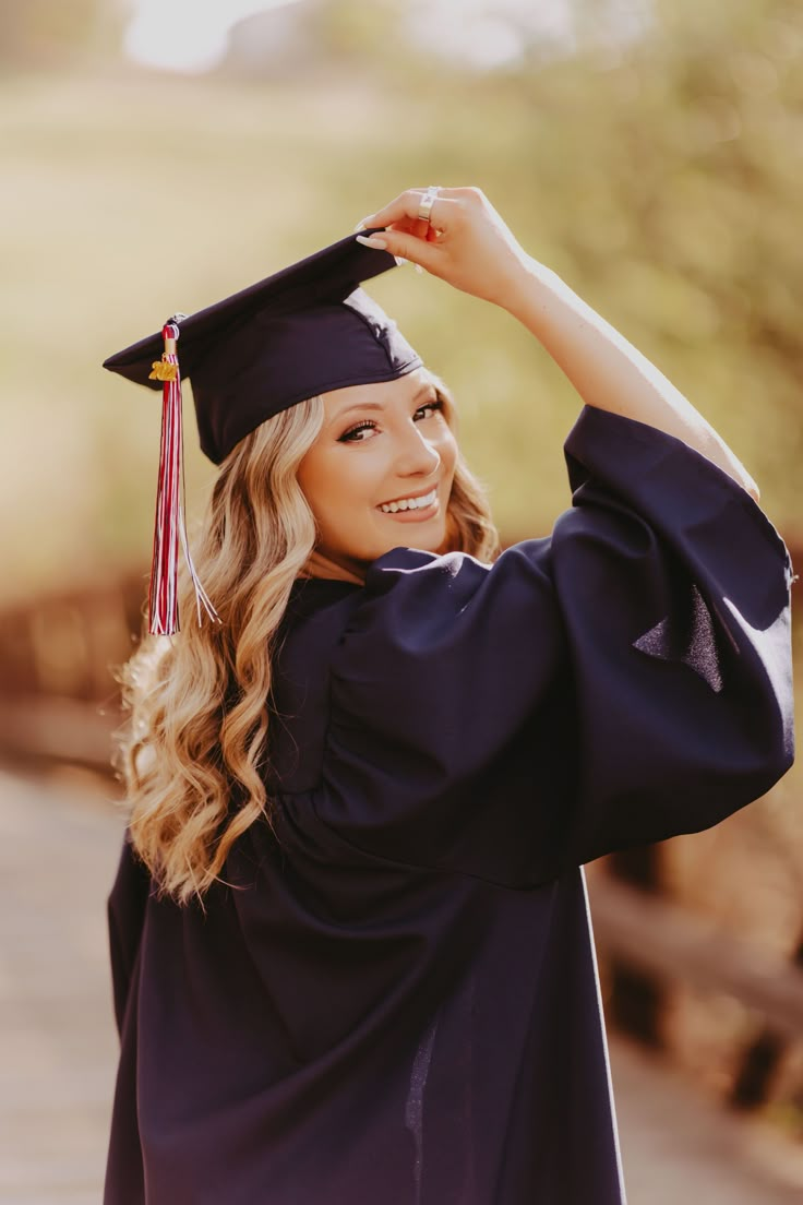 a woman in graduation cap and gown holding her hand up to her head while smiling