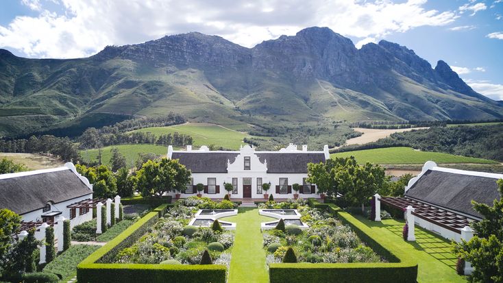 an aerial view of a white house surrounded by greenery and mountains in the background