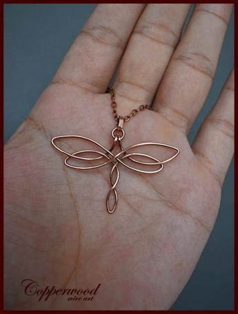 a hand holding a gold dragonfly necklace on it's palm with the word,