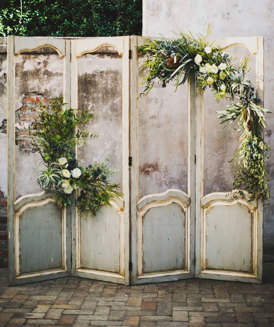 an old screen with flowers and greenery on it, in front of a wall